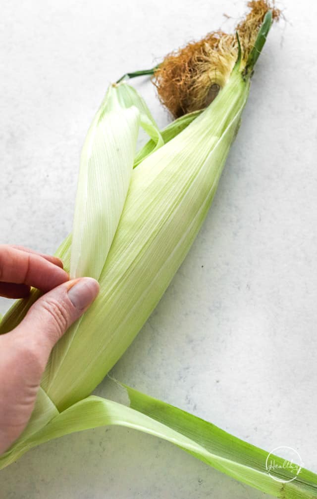 hand peeling husk off corn cob