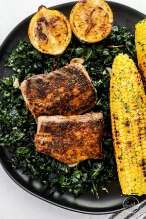 blackened mahi mahi on a plate with kale and grilled corn on the cob