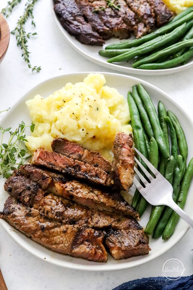 sliced steak on a plate with green beans and mashed potatoes