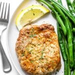 air fryer pork chops on a white plate with green beans and a lemon slice