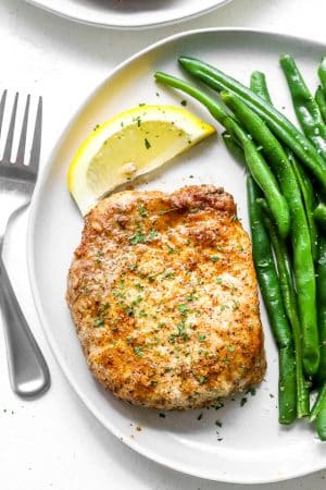 air fryer pork chops on a white plate with green beans and a lemon slice