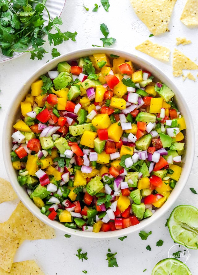 mango salsa in a white serving bowl with tortilla chips and cilantro bunch on the side