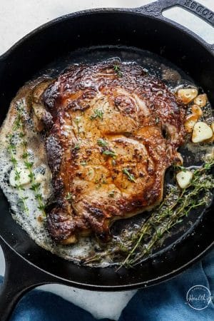 steak cooking in cast iron pan with herbs and melted butter