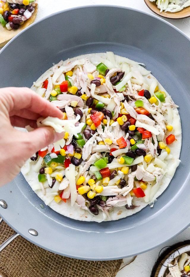 hand sprinkling cheese on open faced quesadilla in a pan