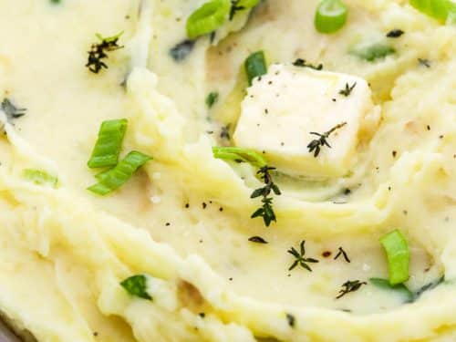 roasted garlic mashed potatoes in a serving bowl with spoon, herbs and a pat of butter