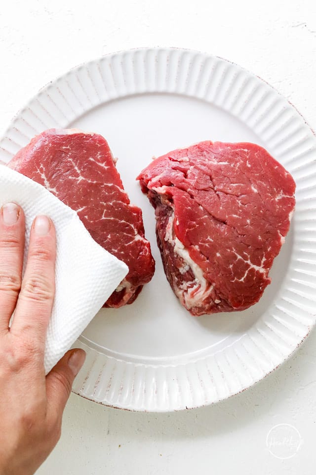 hand patting raw beef with paper towel