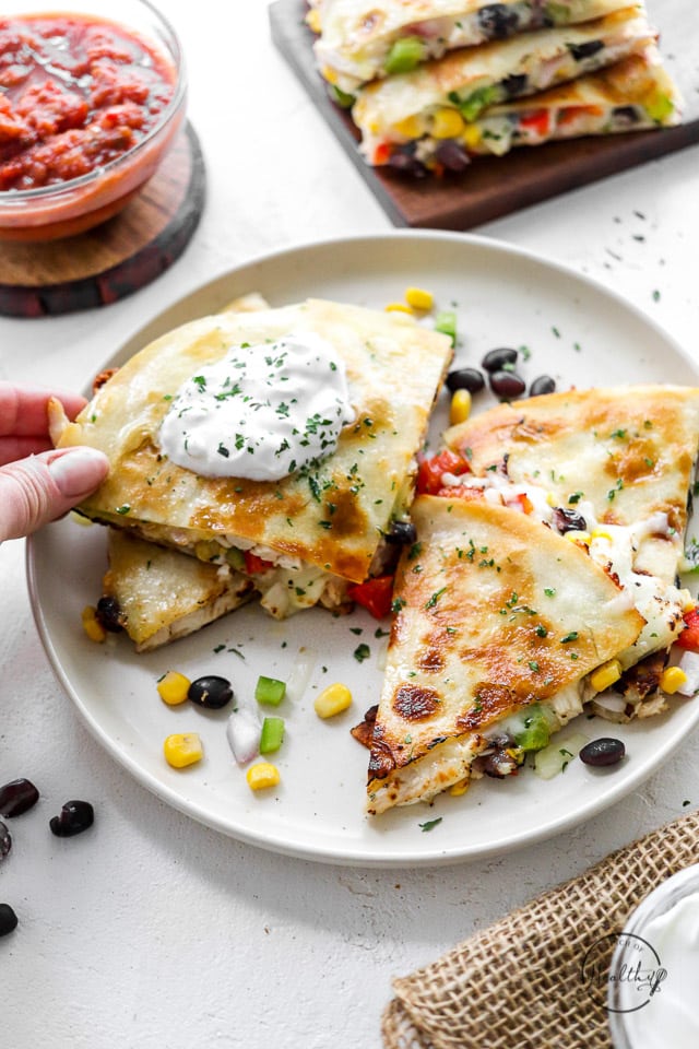 hand grabbing a triangle slice of chicken quesadilla from white plate