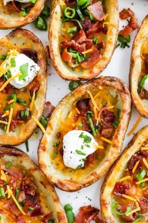 crispy oven baked potato skins with bacon, sour cream, cheese and chives on white surface
