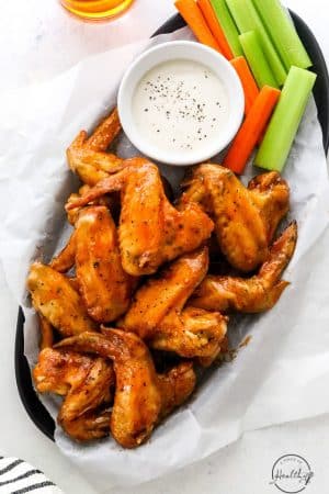 Air fryer buffalo wings in a serving dish with ranch, celery and carrot