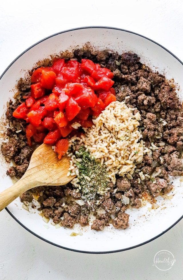 Adding tomatoes and rice to the meat in a pan