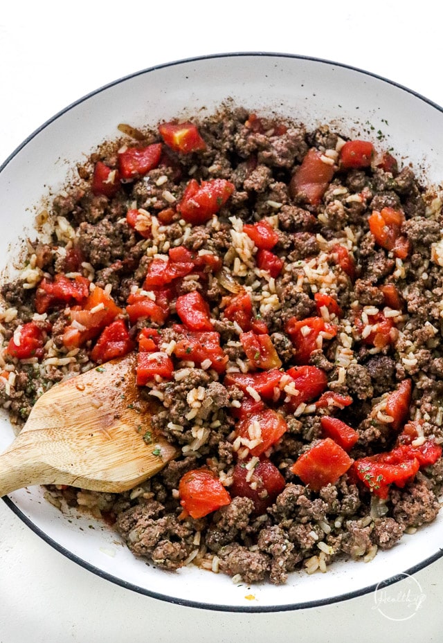 cooking meat and veggies in a pan with wooden spoon
