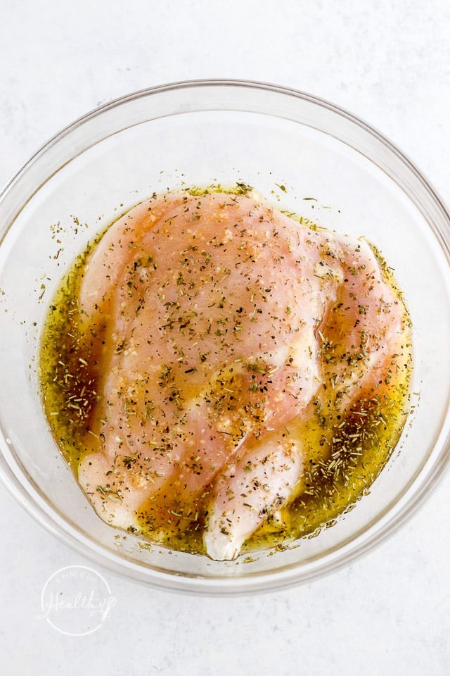 raw chicken breast marinating in a clear glass bowl