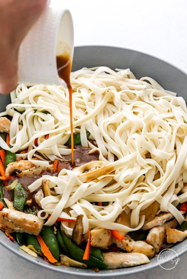 pouring sauce onto chicken lo mein in a pan