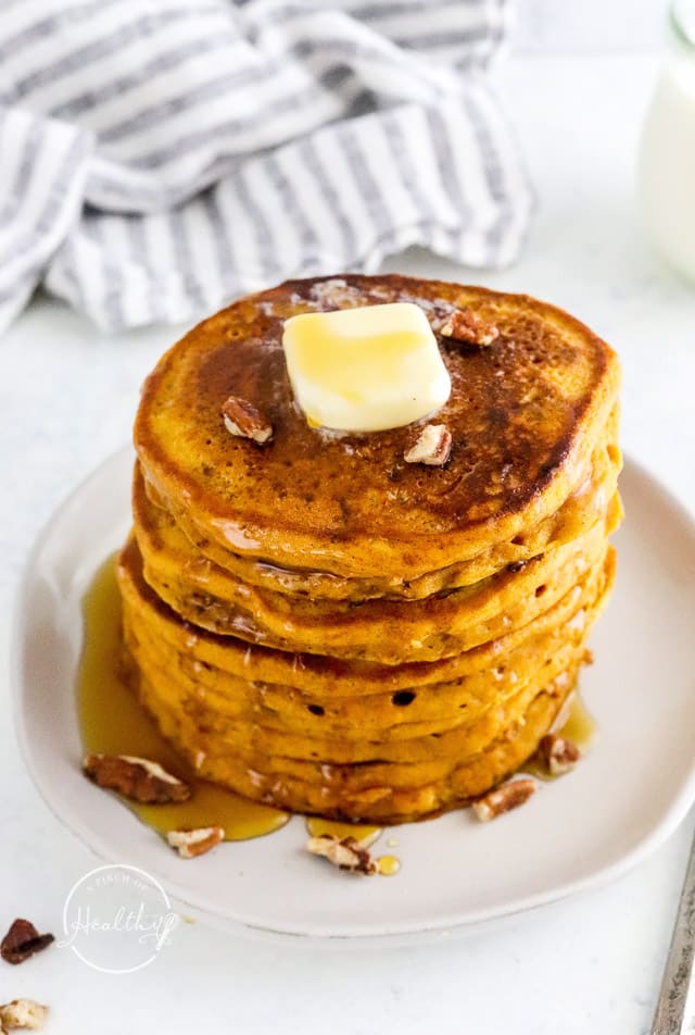 stack of pumpkin pancakes with butter and syrup on a white plate