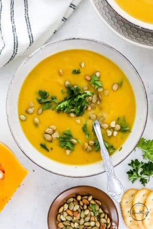Butternut Squash Soup with garnishes in a white bowl with spoon