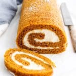 Pumpkin roll with a slice cut on a white surface
