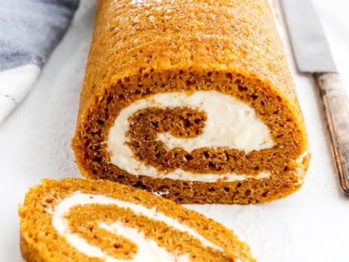 Pumpkin roll with a slice cut on a white surface