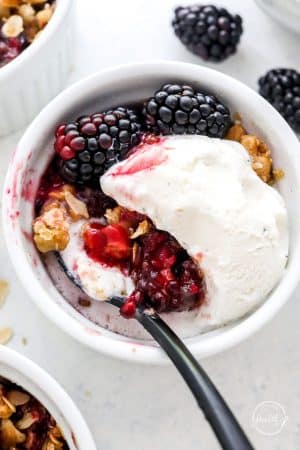 single serving ramekin of blackberry crisp a la mode with spoon