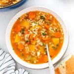 Vegetable barley soup in a white bowl with spoon