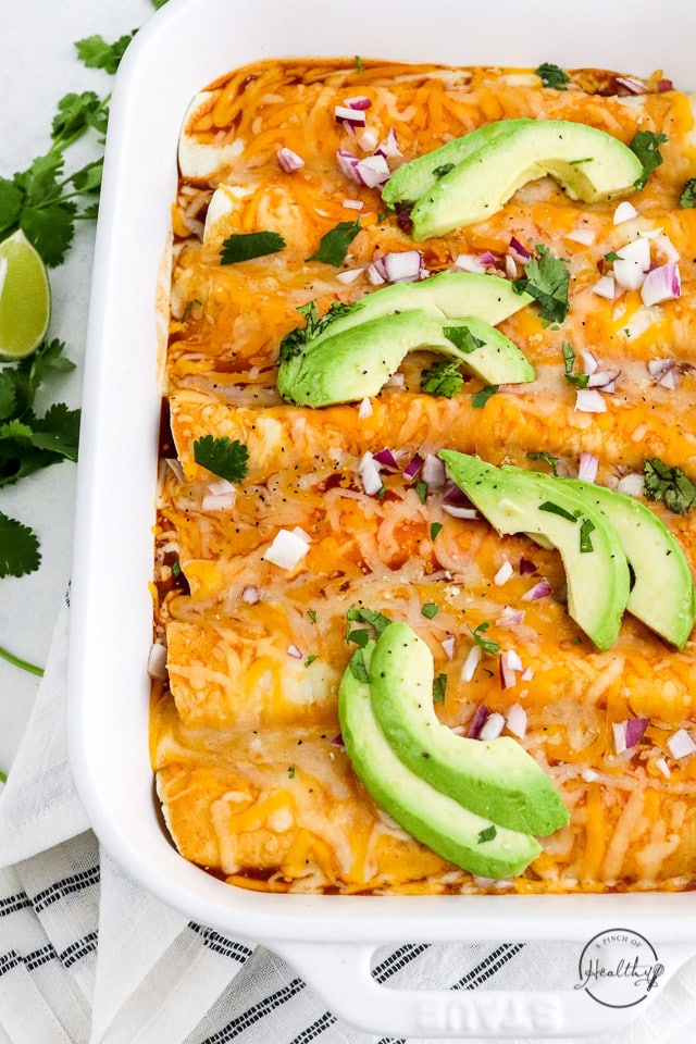 vegetarian enchiladas baked in casserole dish topped with avocado slices