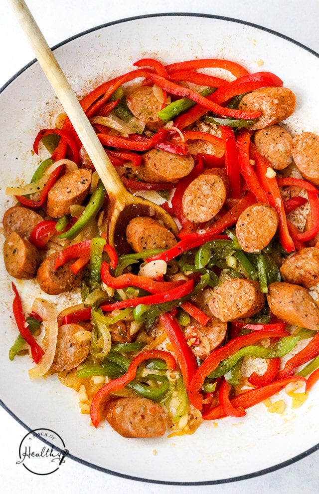 adding sausage to onions and peppers cooking in a skillet