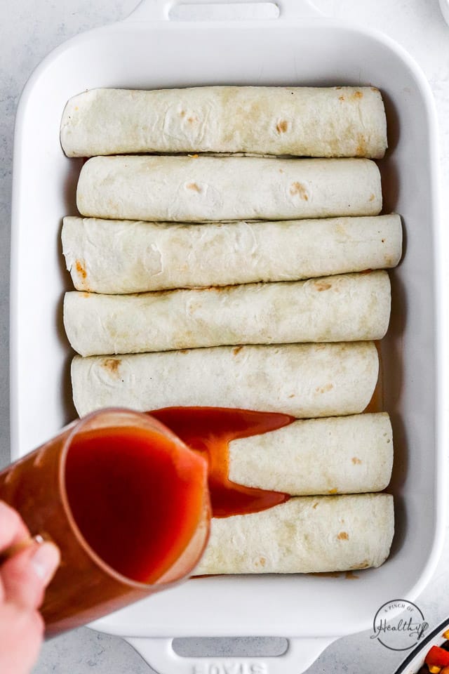 pouring sauce over stuffed and rolled flour tortillas