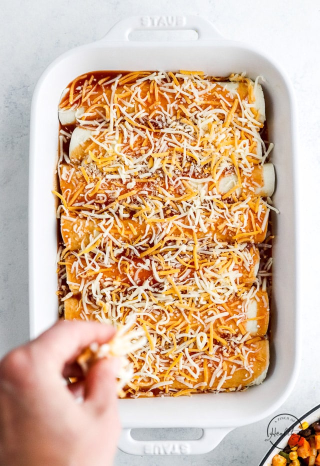 hand sprinkling cheese on top of enchiladas