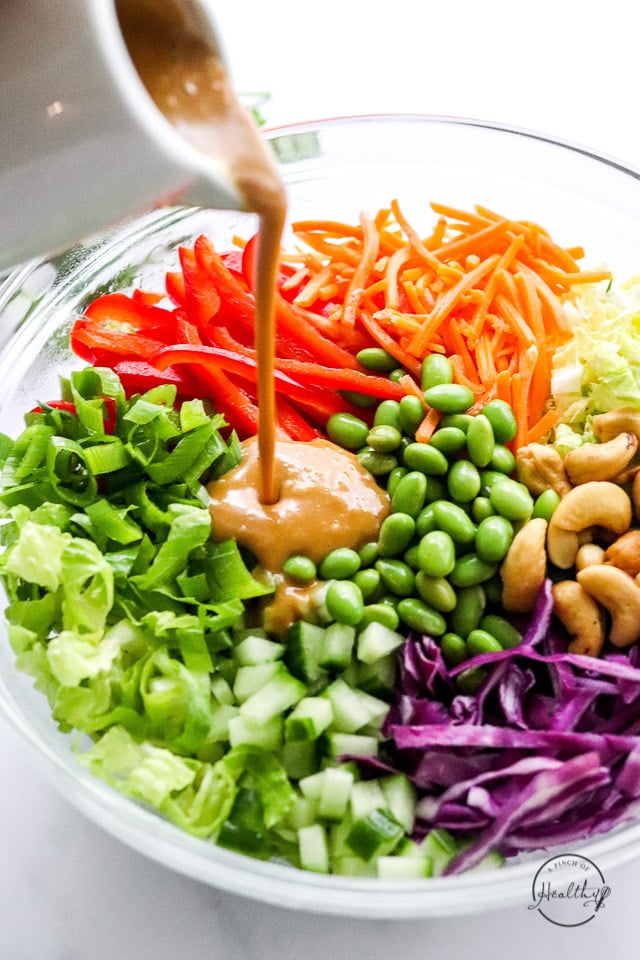 pouring peanut dressing on Thai salad