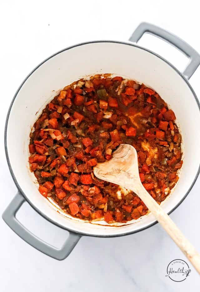 adding tomatoes and spices to a pot