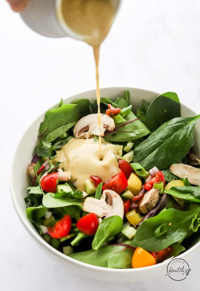pouring tahini dressing on a salad