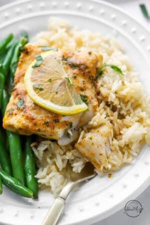 closeup of baked cod on a plate with lemon and green beans