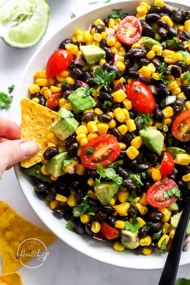 hand dipping black bean salad out with a tortilla chip