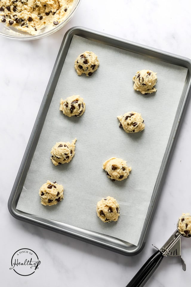 raw cookie dough scooped out on a lined baking sheet