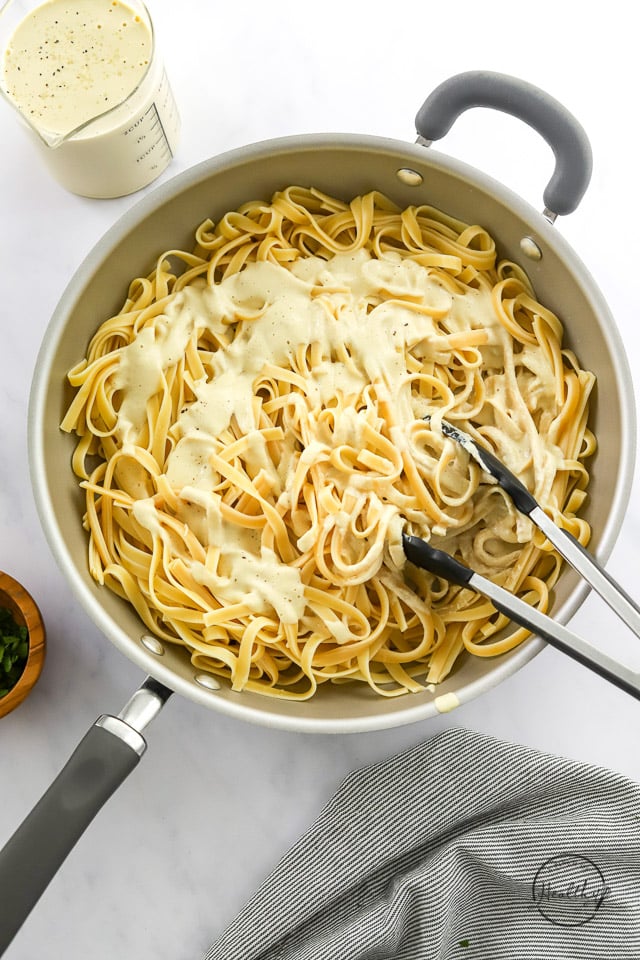 tossing pasta in vegan Alfredo sauce in a pan