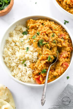 red lentil dal with rice in white bowl with spoon