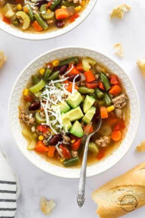 turkey vegetable soup in a white bowl with spoon and shredded cheese