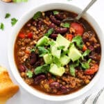 vegan chili in a white bowl with diced avocado and a spoon