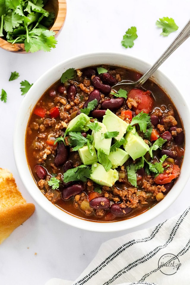 vegan chili in a white bowl with diced avocado and a spoon