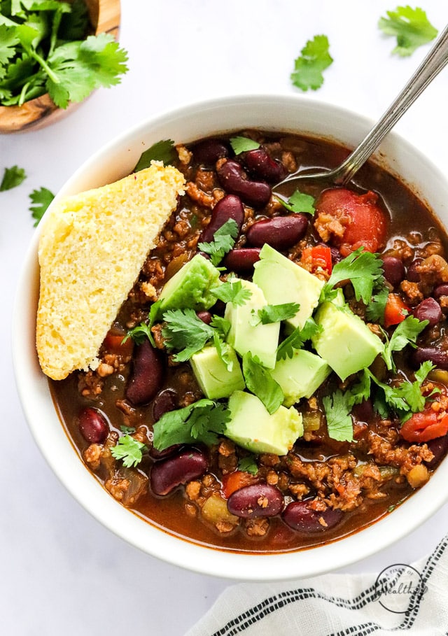 vegan chili in a white bowl with avocado and corn bread