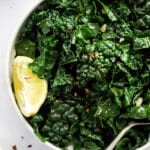 sautéed kale in a serving dish with lemon and spoon