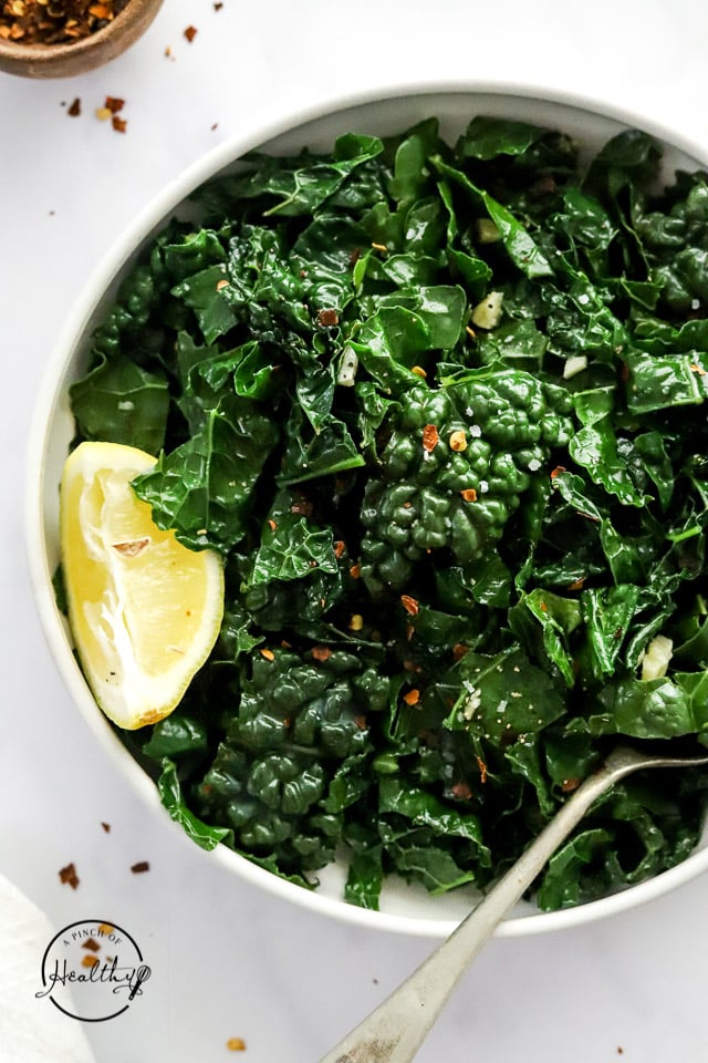 sautéed kale in a serving dish with lemon and spoon