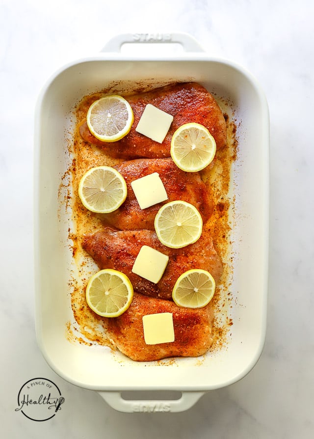 uncooked chicken in a pan with butter and lemon