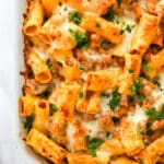 closeup of baked rigatoni with melted cheese in white casserole dish