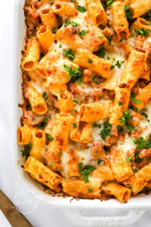 closeup of baked rigatoni with melted cheese in white casserole dish