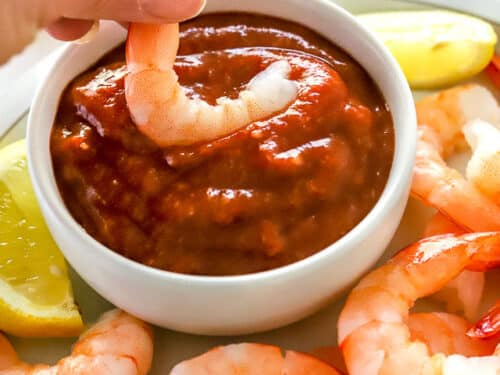 hand dipping shrimp in cocktail sauce
