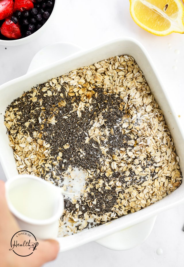 pouring milk over dry ingredients in a baking dish to make baked oatmeal