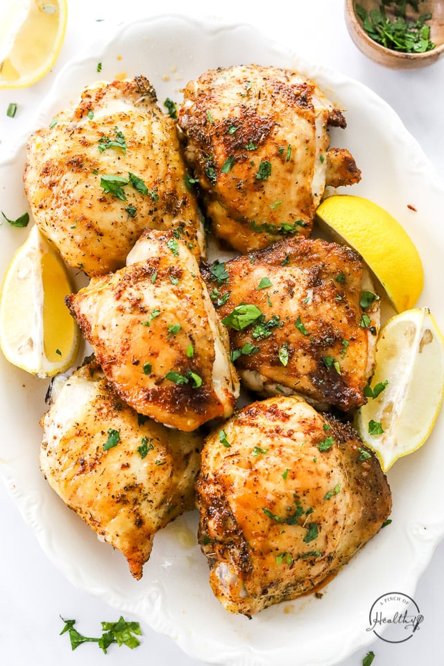 baked chicken thighs on a platter with lemon wedges