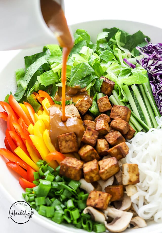 drizzling peanut dressing over Thai noodle salad