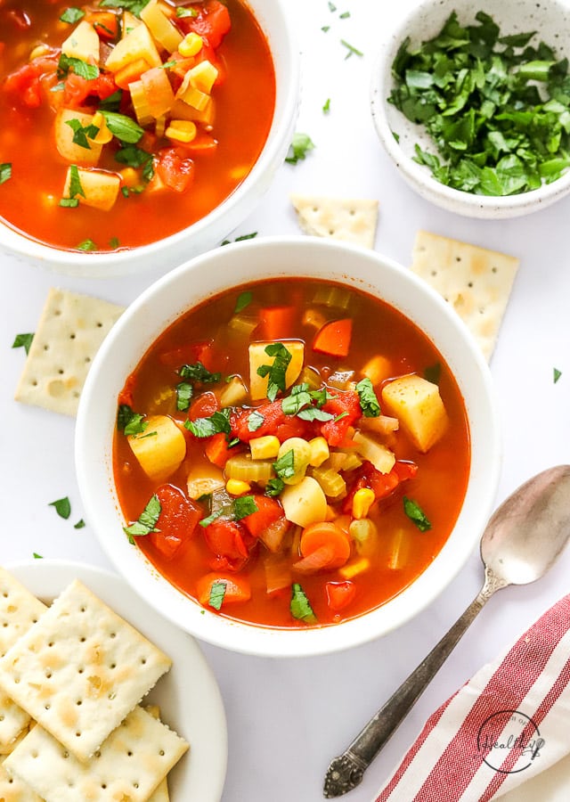 Homemade Vegetable Soup in white bowl with spoon with saltines on the side