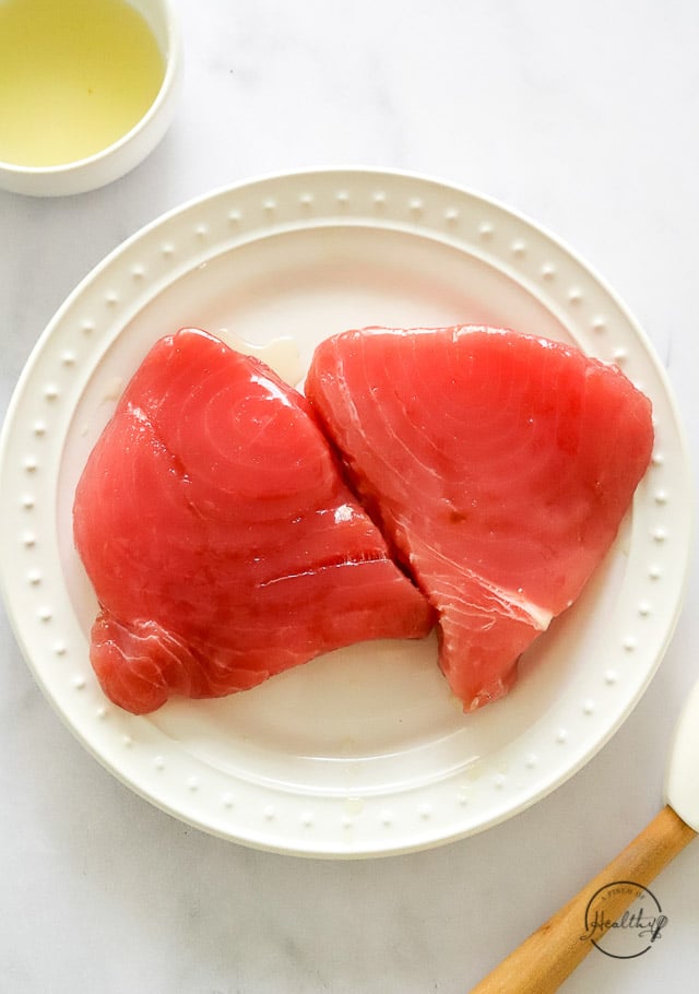 Raw tuna steaks with oil brushed on them on a plate